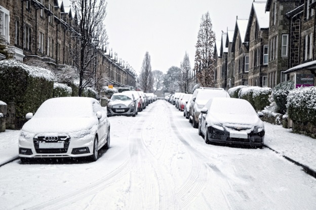 Cars parked on a street lined with row houses, all covered in snow